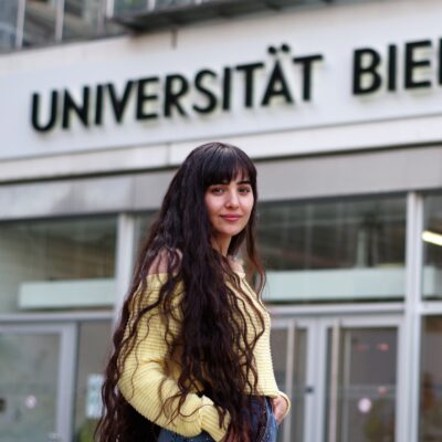 Foto von Ahin Hassaf vor dem Haupteingang der Uni Bielefeld.