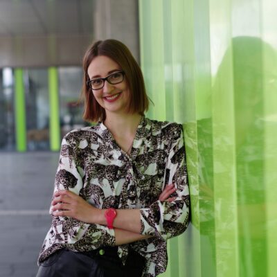 Portät-Bild von Kristina Ising draußen vor dem X-Gebäude, angeleht an grüne Wand.