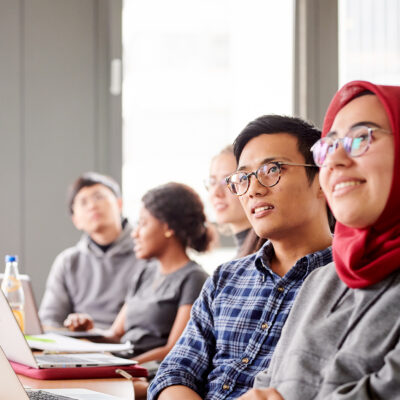 Studierende schauen gebannt auf einen Vortrag mit Laptops vor ihnen.