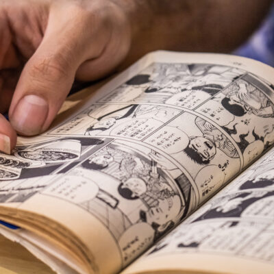 A graphic novel lies on a table, held in one hand