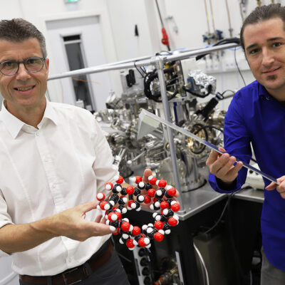 Aufnahme im Physiklabor mit zwei Wissenschaftlern: Professor Dr. Dario Anselmetti von der Universität Bielefeld mit einem Kugelmodell eines Cyclodextrin-Moleküls, Doktorand Niklas Biere mit dem Modell eines Kraftsensors.